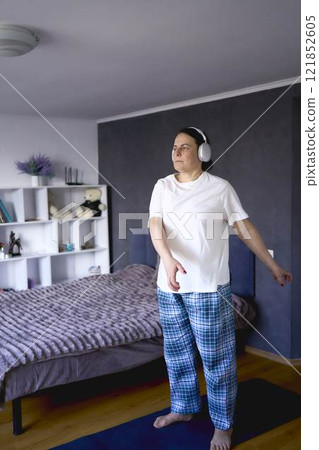 a senior woman doing somatic exercises, yoga at home listening to exercise music in headphones 121852605