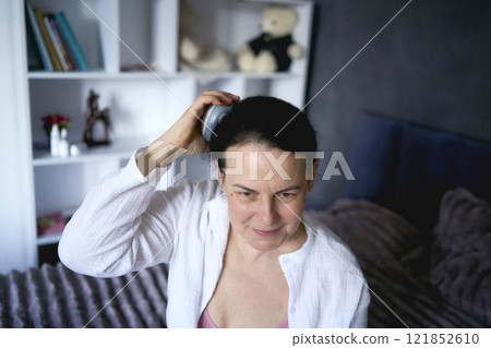 a senior woman massages her head with an electric head and neck massager to stimulate hair growth a senior woman massages her head with an electric head and neck massager to stimulate hair growth 121852610