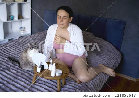 a senior woman in underwear on the bed performs routine self-care with face and body cosmetics a senior woman in underwear on the bed performs routine self-care with face and body cosmetics 121852618