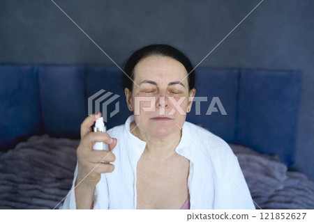 a senior woman in underwear on the bed performs routine self-care with face and body cosmetics , Face Mist, tonic a senior woman in underwear on the bed performs routine self-care with face and body cosmetics , Face Mist, tonic 121852627