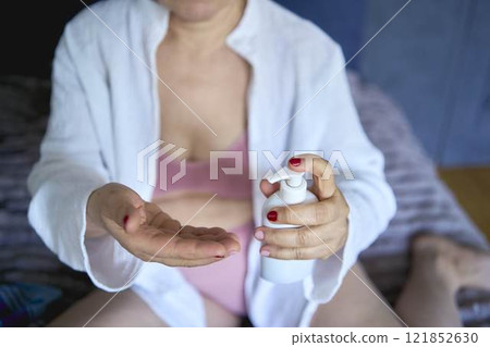 a senior woman in underwear on the bed performs routine self-care with face and body cosmetics a senior woman in underwear on the bed performs routine self-care with face and body cosmetics 121852630