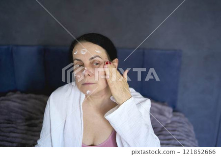 a senior woman in underwear on the bed performs routine self-care with face and body cosmetics a senior woman in underwear on the bed performs routine self-care with face and body cosmetics 121852666