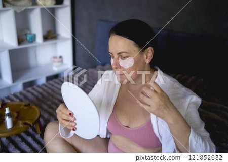 a senior woman in underwear on the bed performs routine self-care with face and body cosmetics a senior woman in underwear on the bed performs routine self-care with face and body cosmetics 121852682