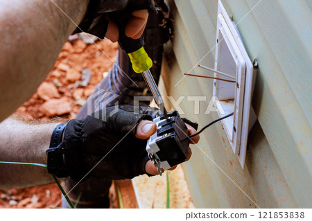 Gloved hand carefully wires a installing new electrical outlet into wall cavity. Gloved hand carefully wires a installing new electrical outlet into wall cavity. 121853838