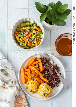 A healthy and filling meal of brown rice, baked sweet potato and squash chickpea pancakes, packed with flavor and nutrients, fresh salad of tomatoes and cucumbers 121853870