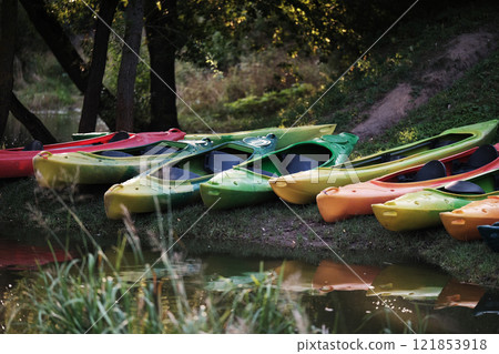 Many canoes of different colors on the river bank before training without people. Boating on the city river Many canoes of different colors on the river bank before training without people. Boating on the city river 121853918