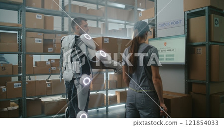 Worker in Powered Exoskeleton Walks with Cardboard Box, Female Logistics Manager Scans Package 121854033