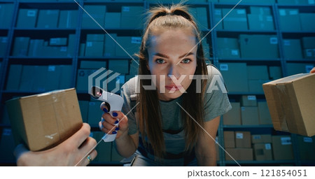 Tired Female Warehouse Employee Looking at Camera, Scanning Cardboard Boxes Using Scanner Tired Female Warehouse Employee Looking at Camera, Scanning Cardboard Boxes Using Scanner 121854051