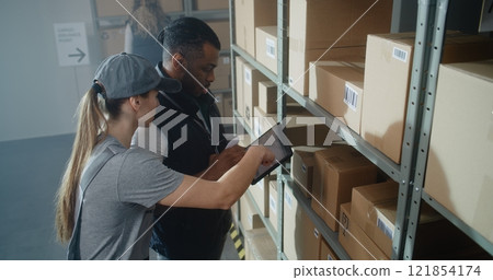 Multiethnic Warehouse Workers Using Tablet Computer, Scanning Cardboard Boxes 121854174