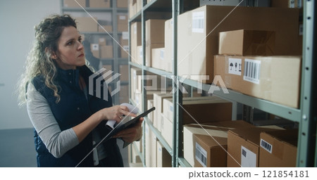 Female Warehouse Associate Scans Cardboard Box, Checks Inventory on Tablet Computer Female Warehouse Associate Scans Cardboard Box, Checks Inventory on Tablet Computer 121854181