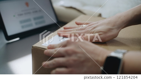 Close Up of Female Shipping and Receiving Clerk Putting Sticker on Cardboard Parcel 121854204