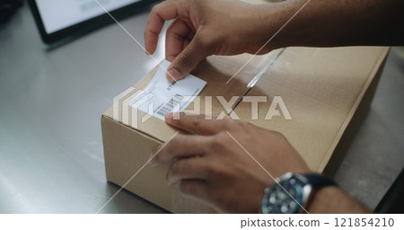African American Warehouse Clerk Putting Sticker on Package, Scanning Code 121854210