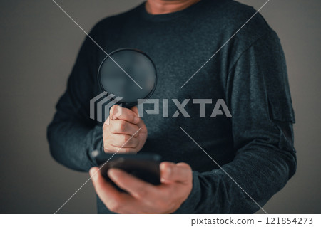 Businessman standing in suit holding magnifying glass and smartphone.Search and research concept. Businessman standing in suit holding magnifying glass and smartphone.Search and research concept. 121854273