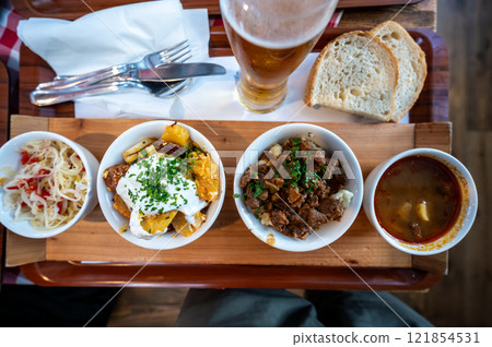 Budapest, Hungary. August 29,2022. Top view footage of an appetizing tasting tray of local delicacies, starting with goulash on the right and going to the left with other dishes with vegetables. Budapest, Hungary. August 29,2022. Top view footage of an appetizing tasting tray of local delicacies, starting with goulash on the right and going to the left with other dishes with vegetables. 121854531