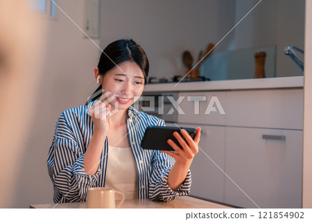晚上在家用智慧型手機觀看運動比賽的年輕女性 晚上在家用智慧型手機觀看運動比賽的年輕女性 121854902