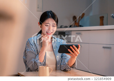 晚上在家用智慧型手機觀看運動比賽的年輕女性 晚上在家用智慧型手機觀看運動比賽的年輕女性 121854909