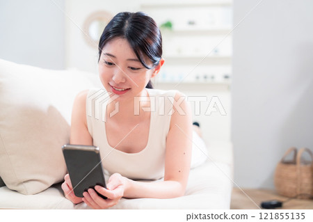 A young woman lying on a sofa and using a smartphone A young woman lying on a sofa and using a smartphone 121855135