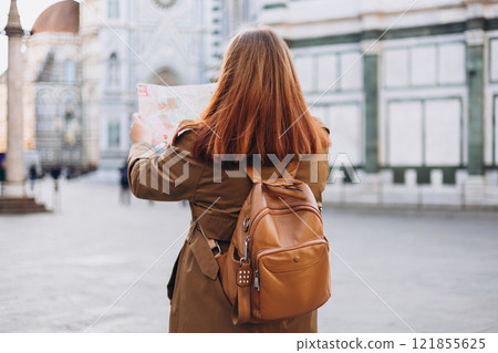 Happy 30s young woman with map in old town in Florence. Holidays and tourism concept. Female tourist searching direction on location map outdoors. Stylish woman visiting Italian landmarks, rear view 121855625
