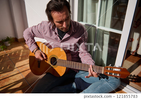 Man playing acoustic guitar on a sunny terrace 121855783