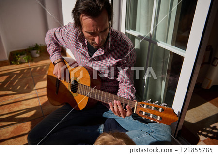 Man playing guitar on balcony in warm sunlight, strumming chords outdoors Man playing guitar on balcony in warm sunlight, strumming chords outdoors 121855785