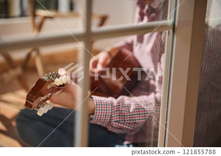 Person playing acoustic guitar on sunny patio with blurred outdoor background Person playing acoustic guitar on sunny patio with blurred outdoor background 121855788
