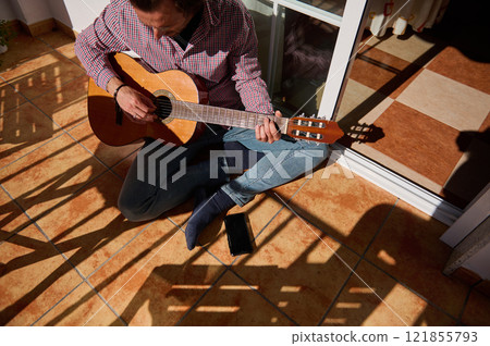Man playing acoustic guitar on a sunny terrace during leisure time Man playing acoustic guitar on a sunny terrace during leisure time 121855793