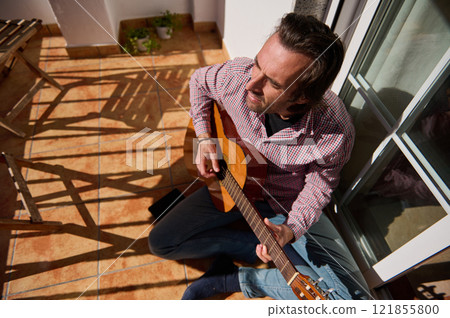 Man enjoying guitar playing on the sunny terrace Man enjoying guitar playing on the sunny terrace 121855800