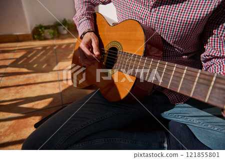 Close-up of a person playing an acoustic guitar on a sunny terrace 121855801