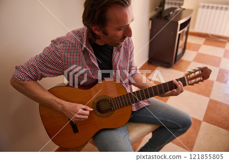 Man playing acoustic guitar in a cozy indoor setting Man playing acoustic guitar in a cozy indoor setting 121855805