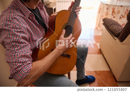 Man playing an acoustic guitar while sitting in a casual indoor environment 121855807