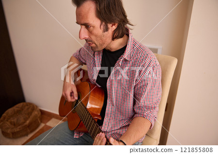 Man playing acoustic guitar in a cozy home setting 121855808