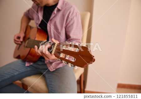 Individual playing an acoustic guitar in a cozy indoor setting Individual playing an acoustic guitar in a cozy indoor setting 121855811