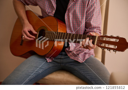 Man playing a classical guitar while sitting indoors relaxedly Man playing a classical guitar while sitting indoors relaxedly 121855812