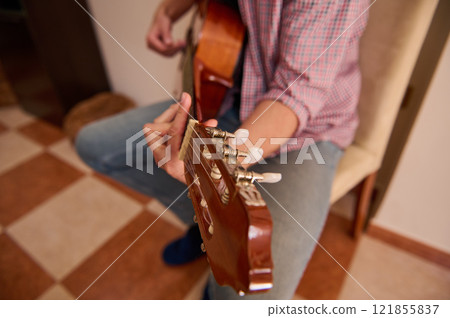 Close-up of a musician tuning a guitar in a home environment Close-up of a musician tuning a guitar in a home environment 121855837