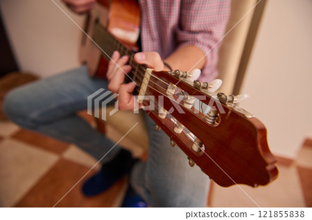 Person strumming an acoustic guitar in a relaxed indoor setting 121855838