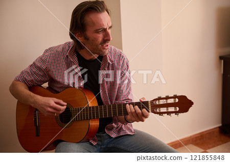 Man playing a classic guitar indoors, expressing concentration and passion for music 121855848