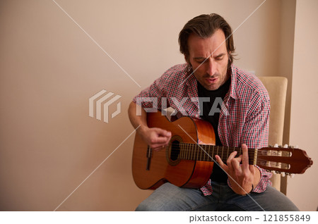 Man sitting on chair playing an acoustic guitar in casual clothes 121855849