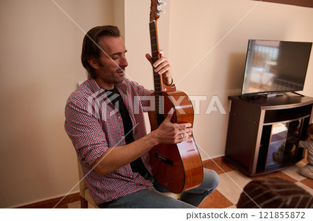 Man playing acoustic guitar indoors in warm lighting during leisure time 121855872