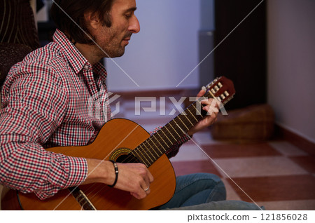 Man playing classical guitar indoors creating a relaxing and musical ambiance Man playing classical guitar indoors creating a relaxing and musical ambiance 121856028