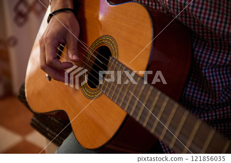 Close-up of a person playing an acoustic guitar indoors Close-up of a person playing an acoustic guitar indoors 121856035