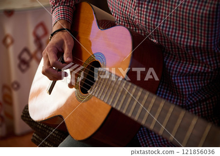 Close-up of a person playing a guitar indoors in natural lighting 121856036