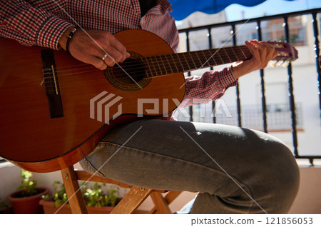 Person playing an acoustic guitar by the balcony in natural light 121856053
