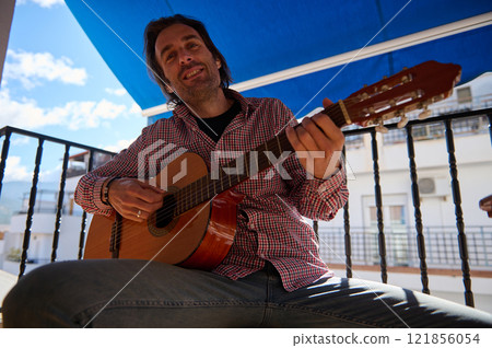 Man playing acoustic guitar outdoors on a sunny day with a blue canopy 121856054