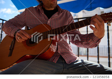 Man playing an acoustic guitar on a sunny day outside on a balcony Man playing an acoustic guitar on a sunny day outside on a balcony 121856058