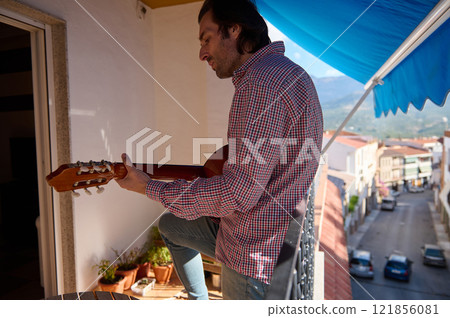 Man playing a guitar on a sunny balcony with a relaxing view 121856081