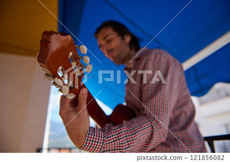 Musician Playing Acoustic Guitar Under Outdoor Shade on a Sunny Day Musician Playing Acoustic Guitar Under Outdoor Shade on a Sunny Day 121856082