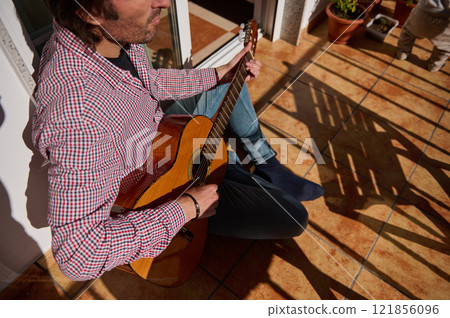 Man playing acoustic guitar outdoors on sunny tiled terrace 121856096