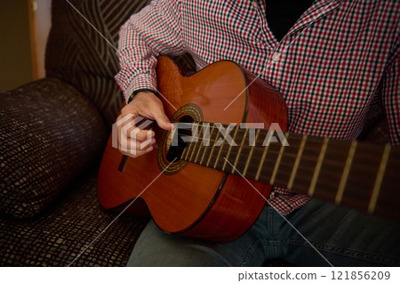 Man playing acoustic guitar in a casual home setting. Man playing acoustic guitar in a casual home setting. 121856209