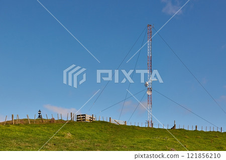 Transmitter tower on a green hill 121856210