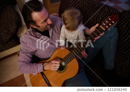 Father and child bonding over acoustic guitar playing at home 121856240